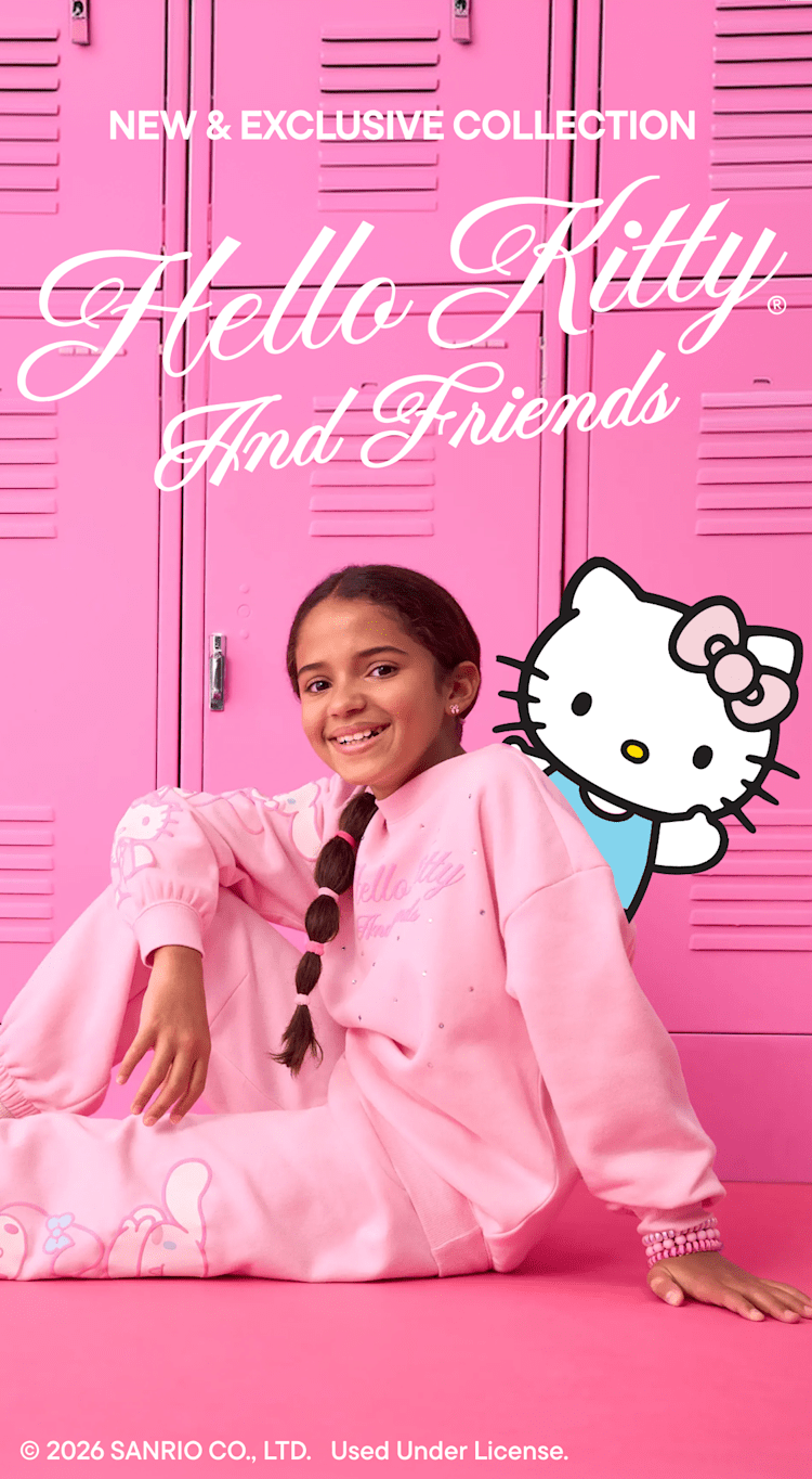 A young child wearing a floral-patterned outfit stands in front of a framed advertisement for a Hello Kitty and Friends Gymboree collection, set against a pink background.
