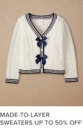 A white cable-knit sweater with navy blue trim and bows, displayed against a beige background.