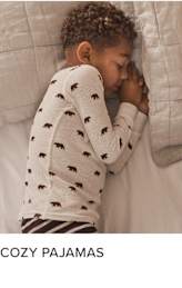 A young child with curly hair is peacefully sleeping on a bed, wrapped in a cozy pajama set with a bear print pattern.