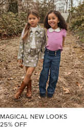 Two young girls, one wearing a camouflage jacket and the other a pink top, stand together in a wooded area with fallen leaves on the ground.