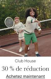 Deux jeunes enfants, un garçon et une fille, jouent au tennis sur un court entouré d'arbres et de verdure.