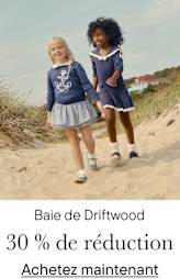 Deux jeunes filles, l'une blonde et l'autre aux cheveux bruns et bouclés, marchent ensemble sur une plage de sable fin avec des dunes en arrière-plan.
