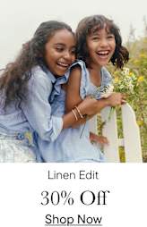 Two young women with curly hair are embracing and laughing joyfully in a field of flowers.