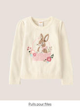 Un jeune garçon aux cheveux bruns bouclés sourit largement, vêtu d'un polo bleu clair à motifs d'étoiles sur fond blanc uni.