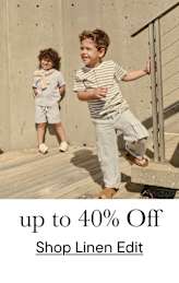 Dos niños pequeños, un niño y una niña, están de pie sobre una terraza de madera frente a un muro de hormigón. El niño lleva una camisa de rayas y la niña un conjunto de color claro. El fondo sugiere un entorno al aire libre.