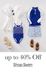 Una colección de diversos trajes de baño y accesorios infantiles, que incluye una blusa blanca, un bañador a rayas, una camiseta de manga larga azul y blanca y un par de sandalias marrones, todo ello dispuesto sobre un fondo liso con el texto superpuesto "hasta un 40 % de descuento".