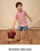 Un jeune garçon vêtu d'une chemise à carreaux rouges et blancs se tient debout sur un plancher en bois, tenant un panier rempli de fraises fraîches.