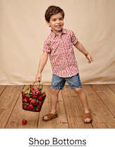 Three young children, two girls and one boy, wearing colorful printed pajamas, are standing together and smiling in a bright, white background.