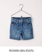 Un short en jean à l'aspect usé et éclaboussé est suspendu à un cintre noir sur un fond blanc uni.