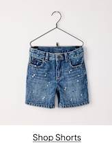 A pair of denim shorts with a distressed, splattered appearance are hanging on a black clothing hanger against a plain white background.