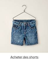 Un short en jean à l'aspect usé et éclaboussé est suspendu à un cintre noir sur un fond blanc uni.