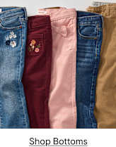 Five pairs of children's pants, featuring embroidered details and a bow, are neatly arranged in the foreground against a plain white background.