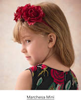 A young girl wearing a red floral headband and a floral dress poses against a neutral, textured background.