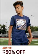 A young person wearing a navy blue t-shirt with a graphic design stands on a sports field with a track and goal posts visible in the background.