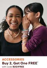 Two young women with warm, friendly expressions are smiling and interacting with each other in the foreground, while a promotional advertisement for accessories is visible in the background.