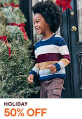 A smiling young person with curly hair stands in front of a festive holiday display with red poinsettia flowers.