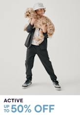 A young person wearing a black jacket and holding a large, fluffy brown dog, standing against a plain white background with text advertising an active sale offering up to 50% off.