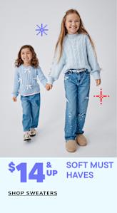 Two young girls wearing denim jeans and light blue sweaters are standing together and smiling, with a text overlay advertising sweaters for $14 and up.