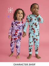 Two young children, a boy and a girl, are standing together in colorful pajamas against a pink background. The boy is wearing a blue pajama set with a pattern of cartoon characters, while the girl is wearing a purple pajama set with a different cartoon character pattern. Both children are smiling and appear to be having fun.