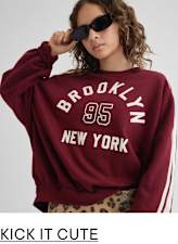 A young woman wearing a burgundy sweatshirt with "Brooklyn 95 New York" printed on it, paired with leopard print pants, stands against a plain background while wearing sunglasses.