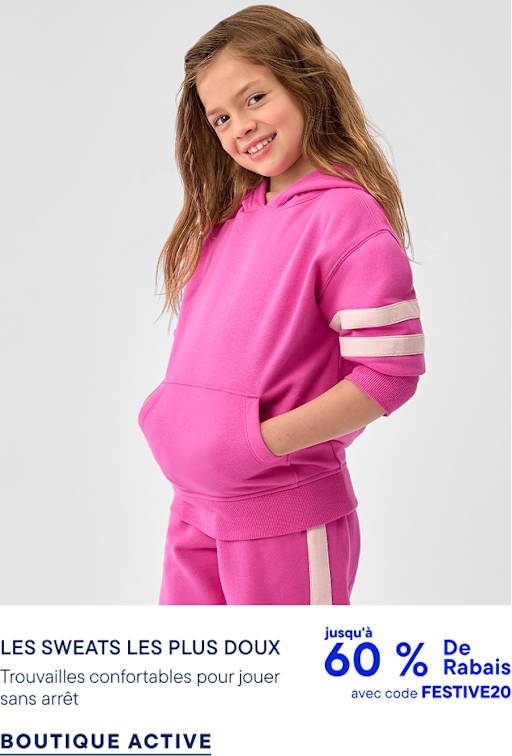 Une jeune fille vêtue d'un sweat à capuche rose vif et d'un pantalon de survêtement assorti se détache sur un fond gris clair uni.