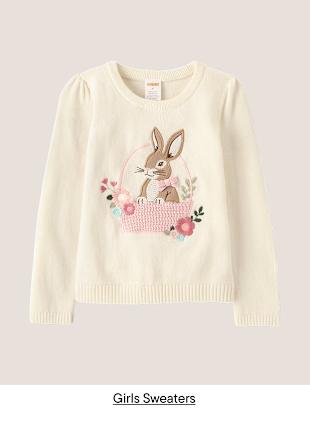 Un suéter color crema con una linda ilustración de un conejito y un diseño floral, sobre un fondo liso.