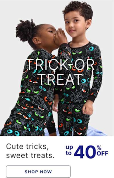 Two young children, a boy and a girl, wearing matching Halloween-themed pajamas and embracing each other affectionately. The background is a plain white backdrop, allowing the focus to remain on the children's playful interaction.