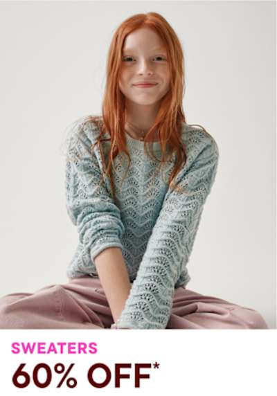 The image shows a young woman with vibrant red hair wearing a patterned sweater and sitting on a plain background. She has a warm, friendly expression on her face.