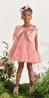 Una joven que viste un vestido de tul rosa se encuentra en medio de un exuberante y verde jardín lleno de flores vibrantes.