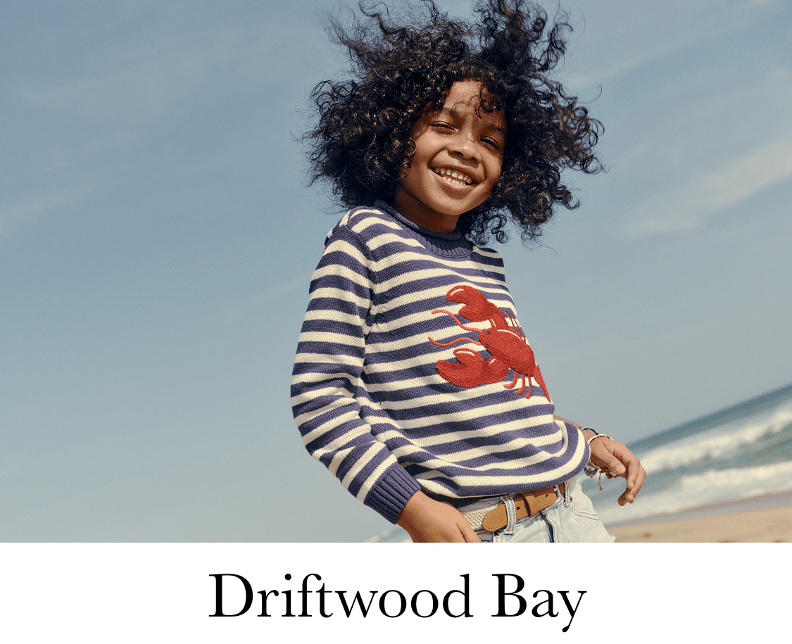 The image shows a young woman with curly hair walking on a sandy beach, with a coastal landscape in the background. She is wearing a striped shirt and appears to be smiling.