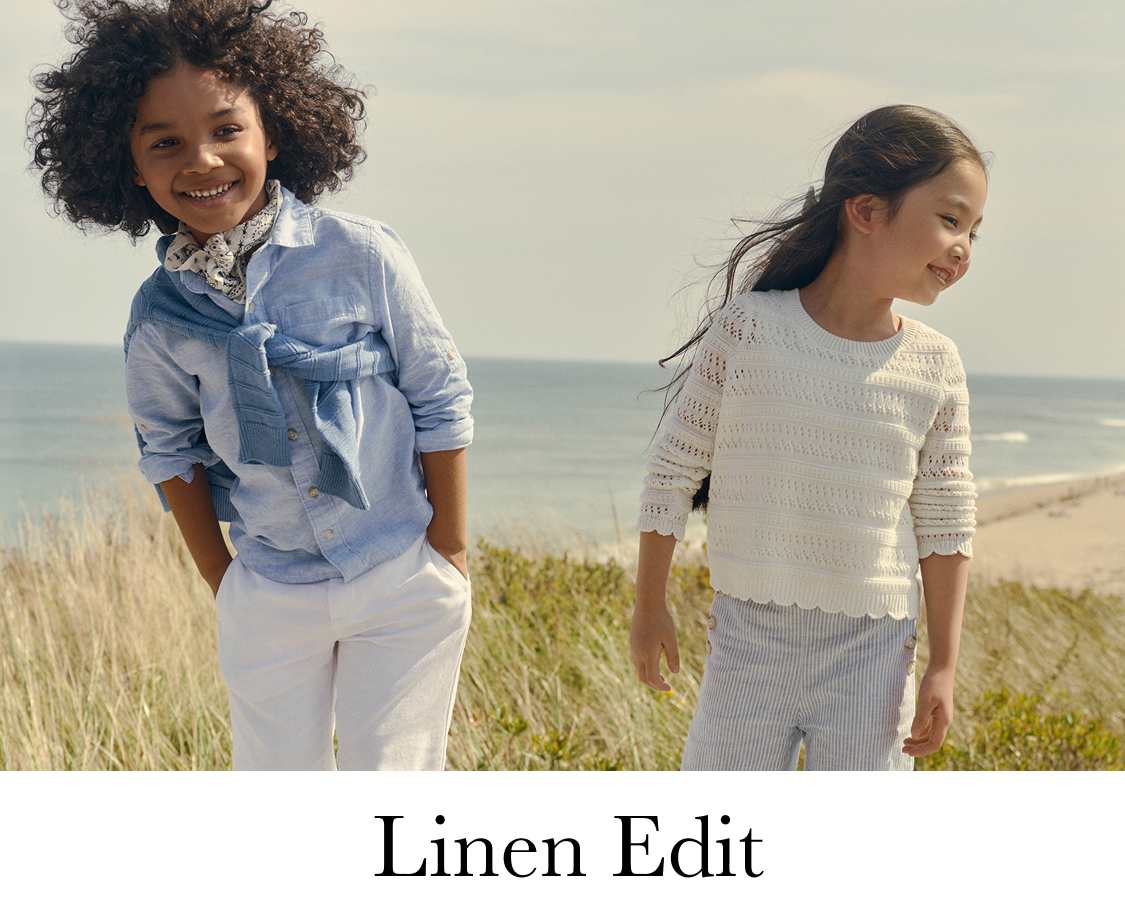 Two young girls with curly hair are laughing and playing in a grassy field, with a city skyline visible in the background.