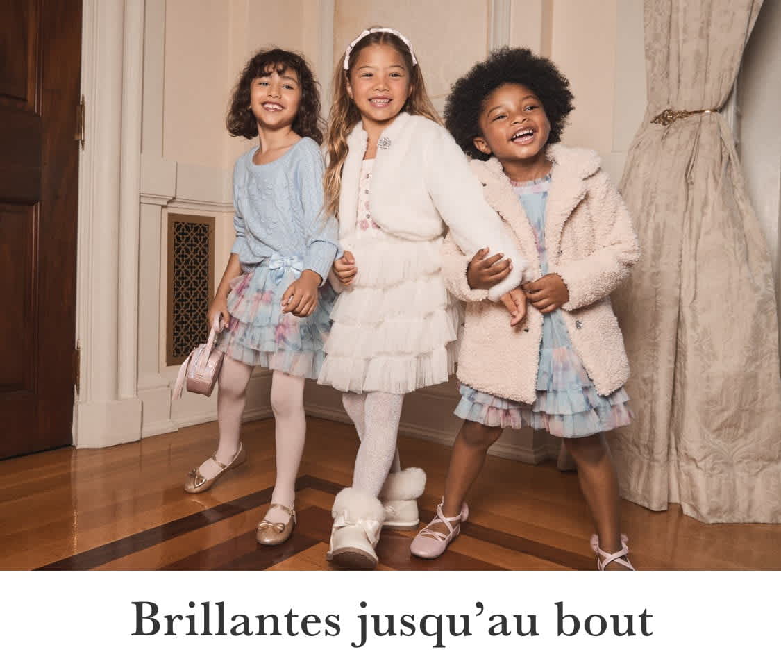 Trois jeunes filles aux cheveux bouclés se tiennent ensemble et sourient, avec un sac à main matelassé rose au premier plan.