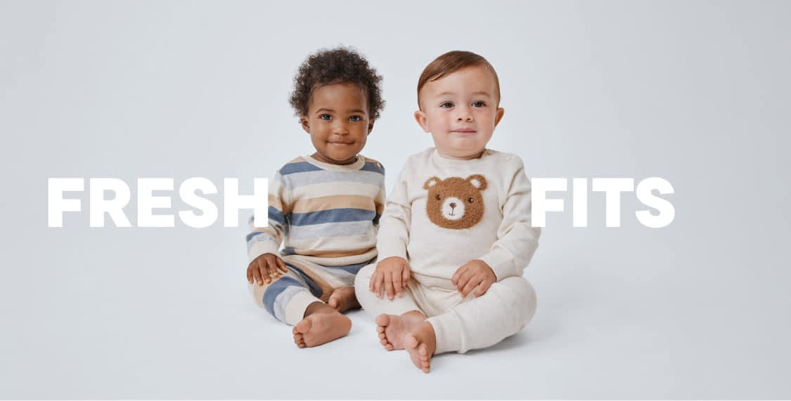 The image shows two young children, a boy and a girl, sitting together on a plain white background. The boy is wearing a striped sweater, while the girl is wearing a sweater with a bear design. Both children have a friendly and relaxed expression on their faces.