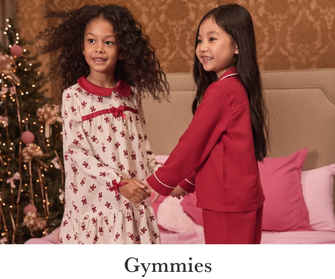 Two young girls wearing vibrant red and pink outfits stand together, their expressions conveying a sense of joy and playfulness. In the background, a soft, pink-hued fabric creates a warm and inviting atmosphere.