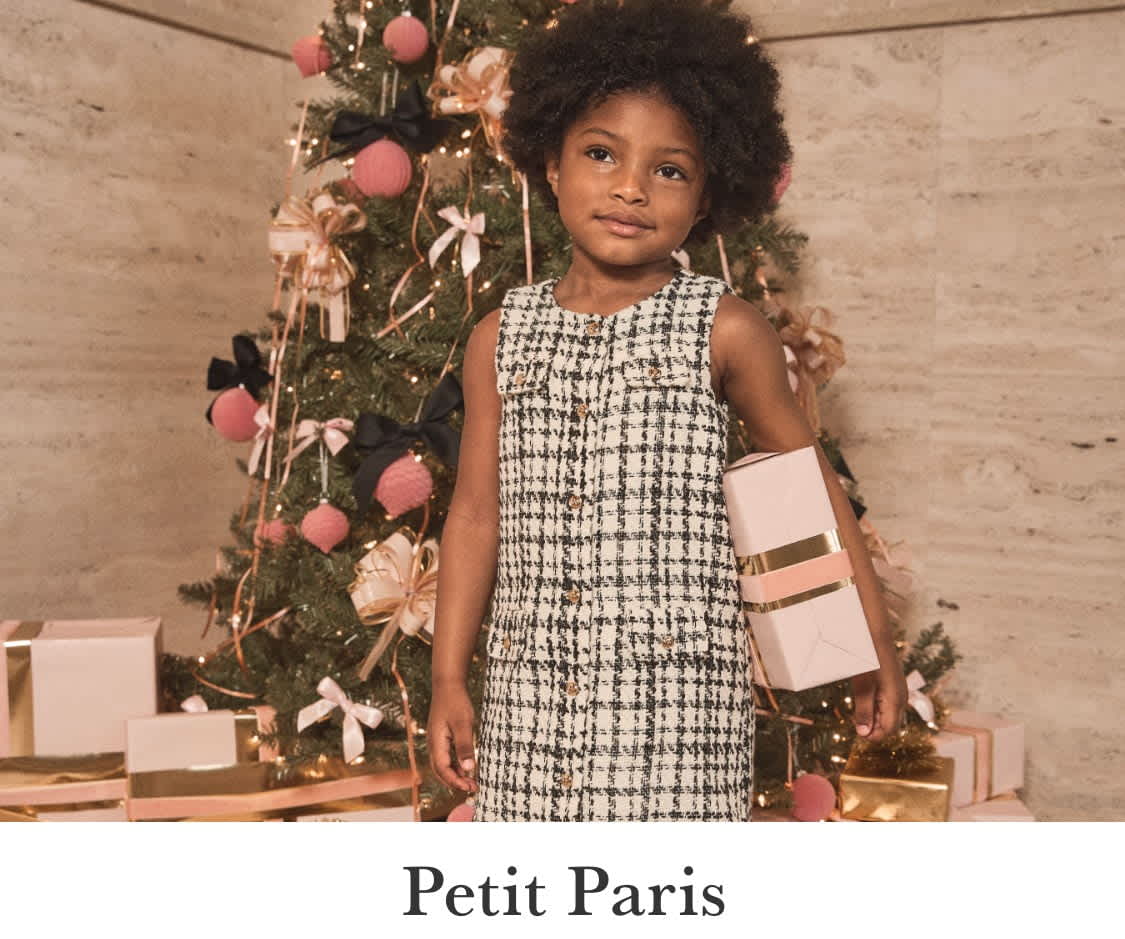 La imagen muestra una escena navideña festiva con una niña en primer plano, rodeada de un árbol de Navidad decorado y otras decoraciones navideñas, mientras que en el fondo se ven otras dos niñas.