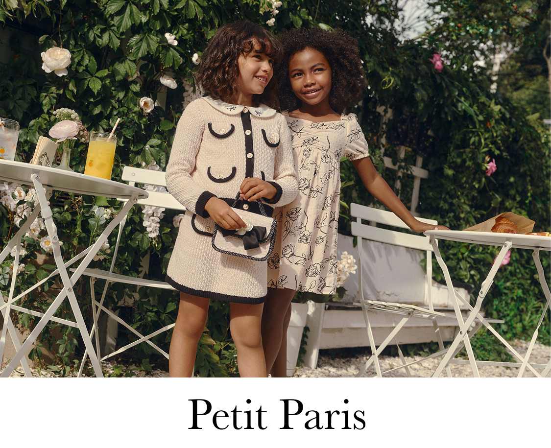 A young woman with long, wavy hair is drinking from a straw in a cup, surrounded by lush greenery and foliage in the background.