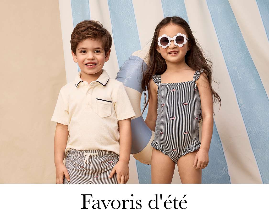 Deux jeunes filles aux cheveux bouclés, l'une portant une chemise bleu marine et l'autre un haut rose, se tiennent debout dans une pièce avec des plantes en pot en arrière-plan.