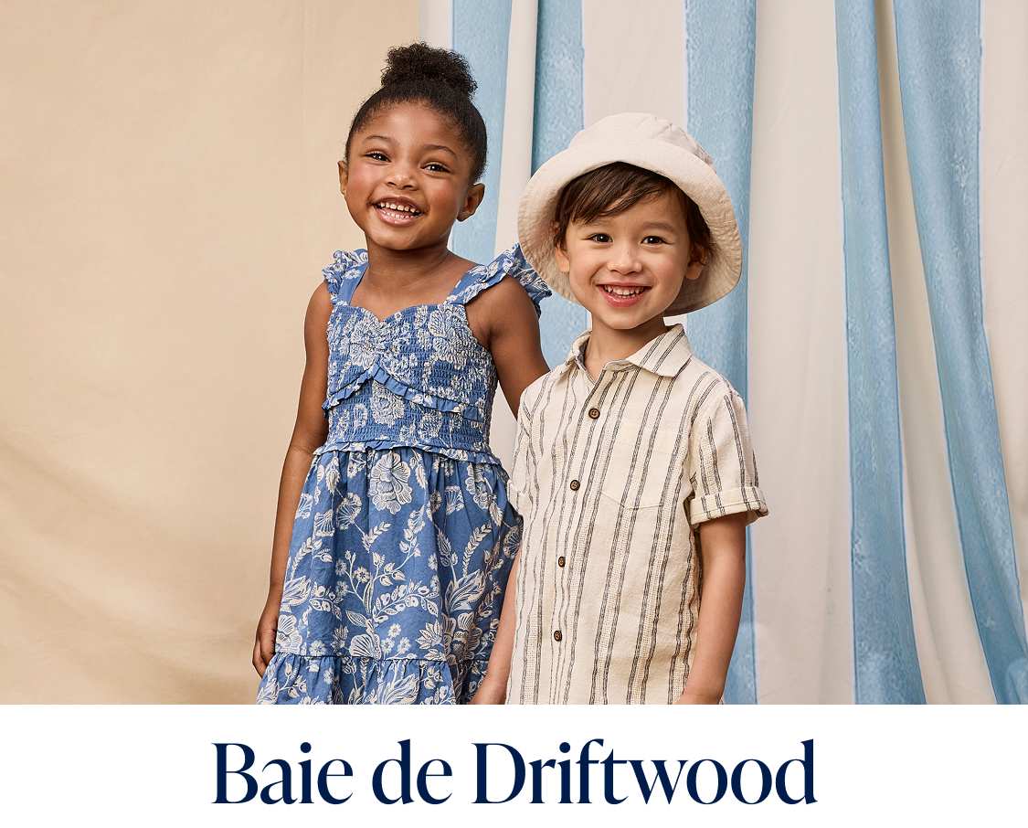 Deux jeunes filles, l'une vêtue d'une robe blanche et l'autre d'une robe lavande, se tiennent debout sur un plancher en bois devant des rideaux bleus et blancs.