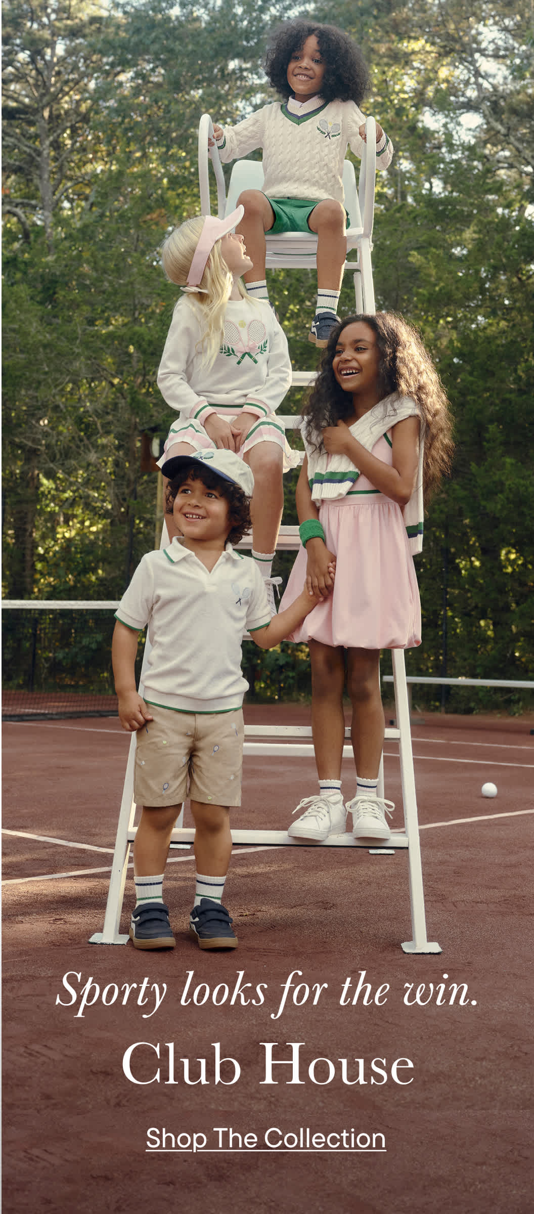 The image depicts a group of young children, both boys and girls, posing together on a tennis court surrounded by lush greenery.