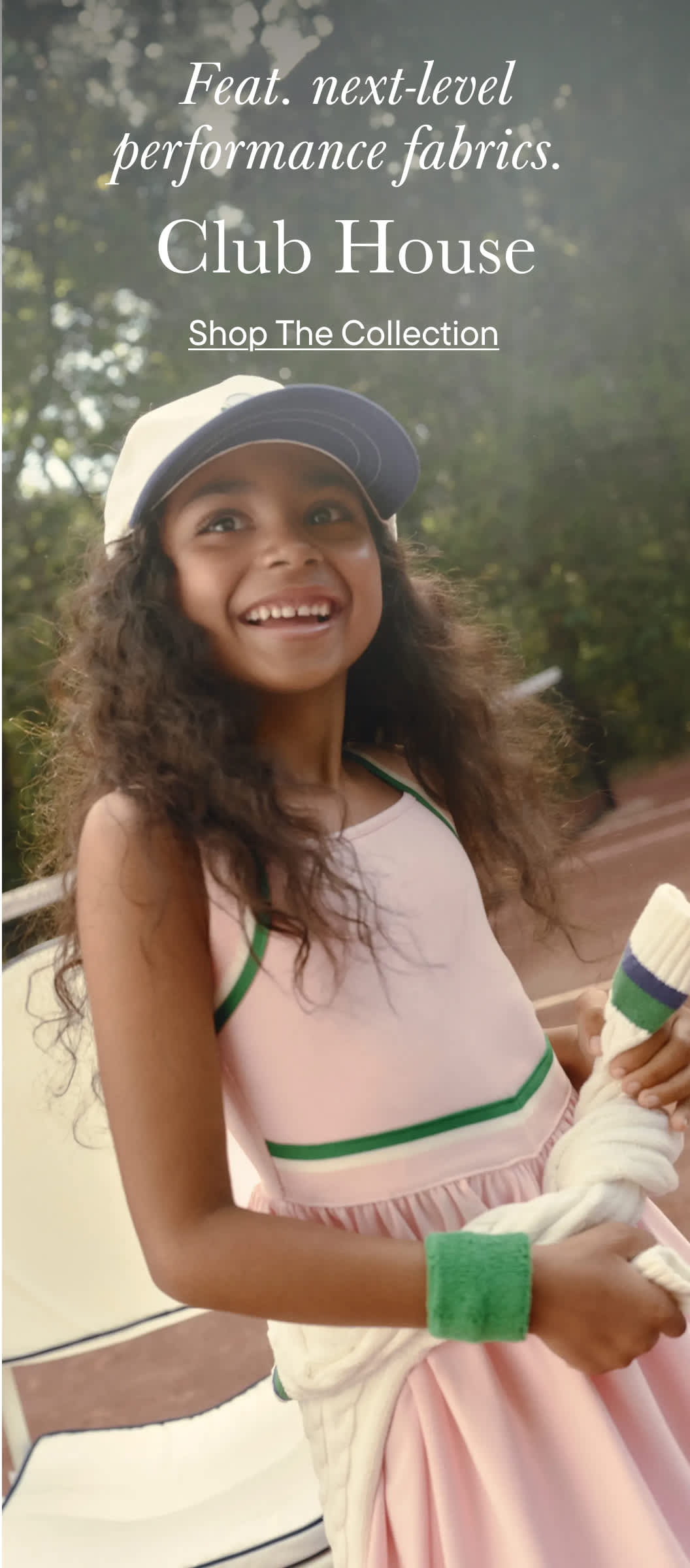 A smiling young woman wearing a pink top and a baseball cap stands in a grassy outdoor setting, surrounded by trees and a sign for "Club House" and "Shop The Collection".