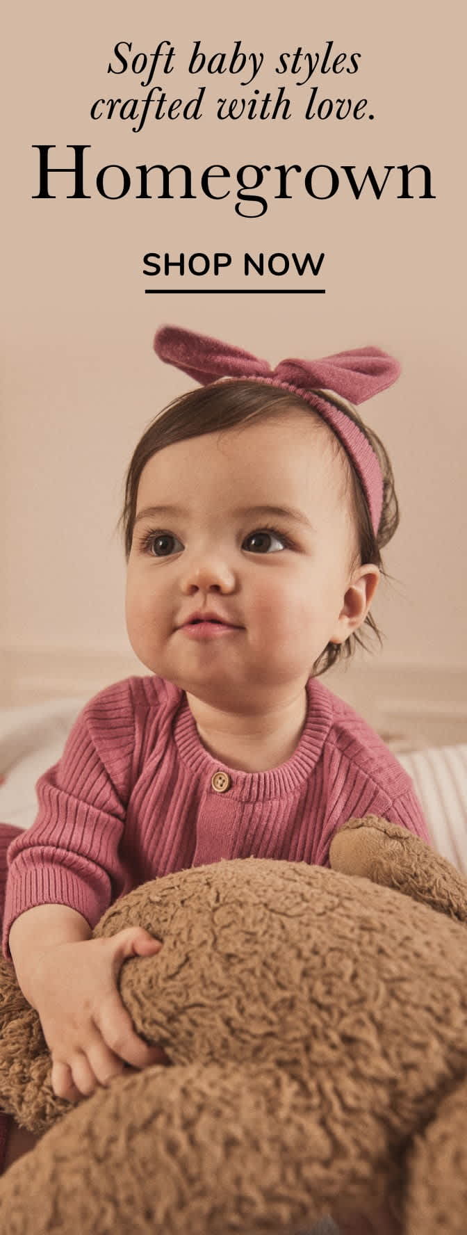 Une petite fille souriante portant un pull rose et un bandeau rose, assise sur une couverture beige avec le texte « Homegrown Shop Now » affiché ci-dessus.