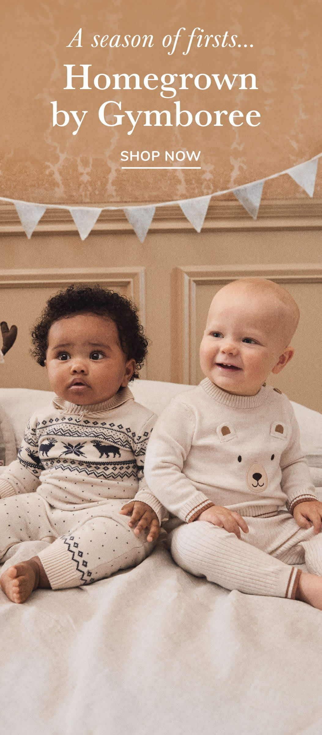Two young children, a boy and a girl, are sitting on a bed surrounded by decorative elements such as a banner and hearts. The background appears to be a bedroom setting with a wooden door frame visible.