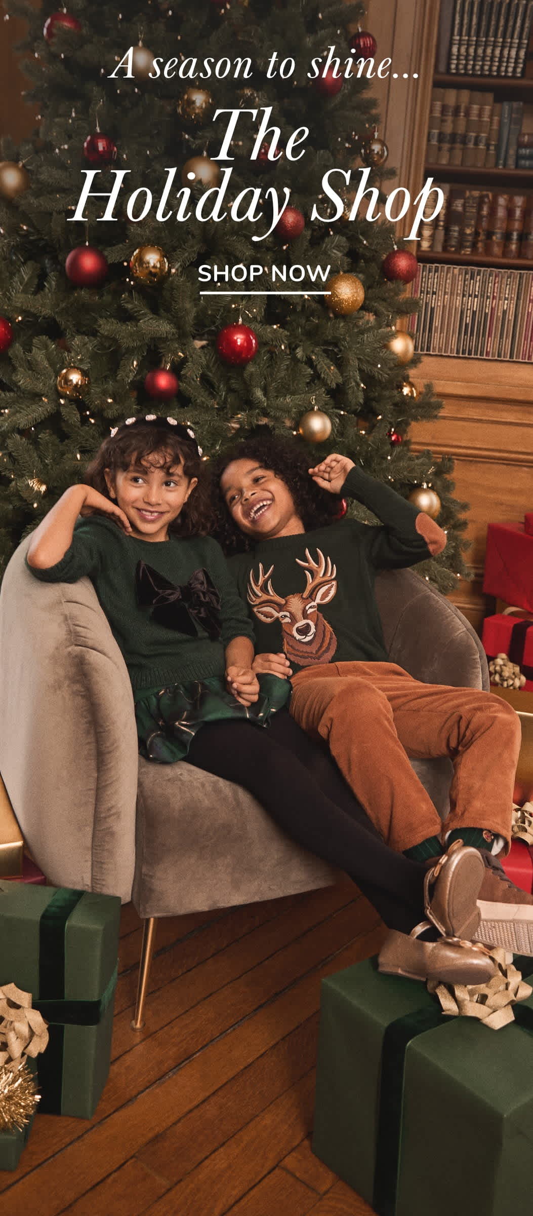 The image shows two people, a man and a woman, sitting on a couch in front of a Christmas tree with holiday decorations and a sign for "The Holiday Shop" in the background.