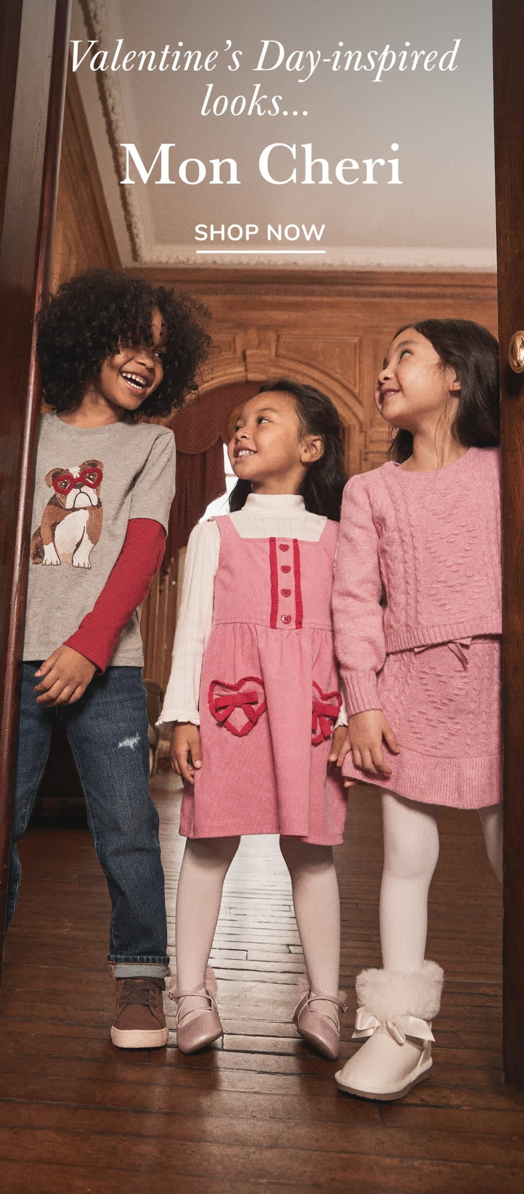 La imagen muestra a tres niñas, dos de las cuales llevan suéteres rosas y rojos, paradas frente a un fondo de madera con un anuncio de "Mon Cheri".