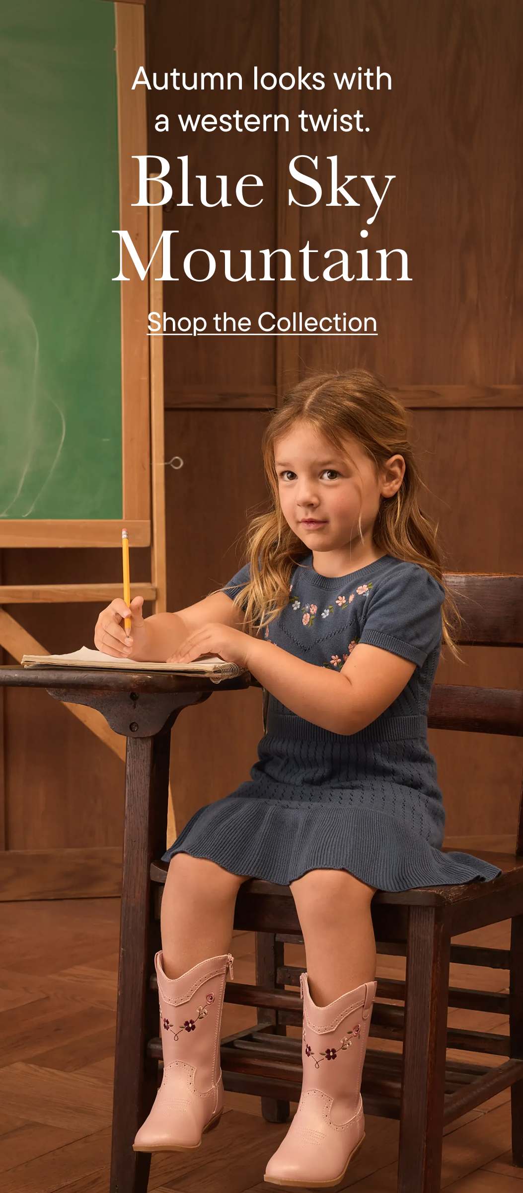 A young girl in pink cowboy boots sits at a desk with a pencil in her hand, in front of a classroom blackboard.