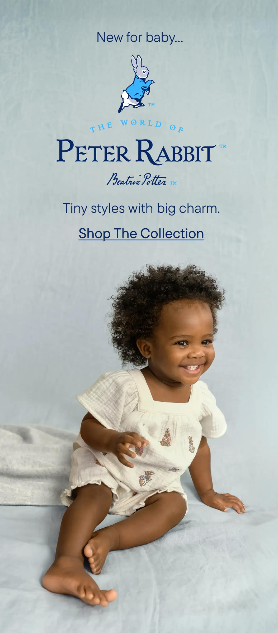 Una niña pequeña, probablemente una niña, está sentada sobre una superficie blanca y sonríe a la cámara. El fondo muestra un cielo azul y el texto "El mundo de Peter Rabbit" junto con el eslogan "Estilos pequeños con gran encanto. Compra la colección".