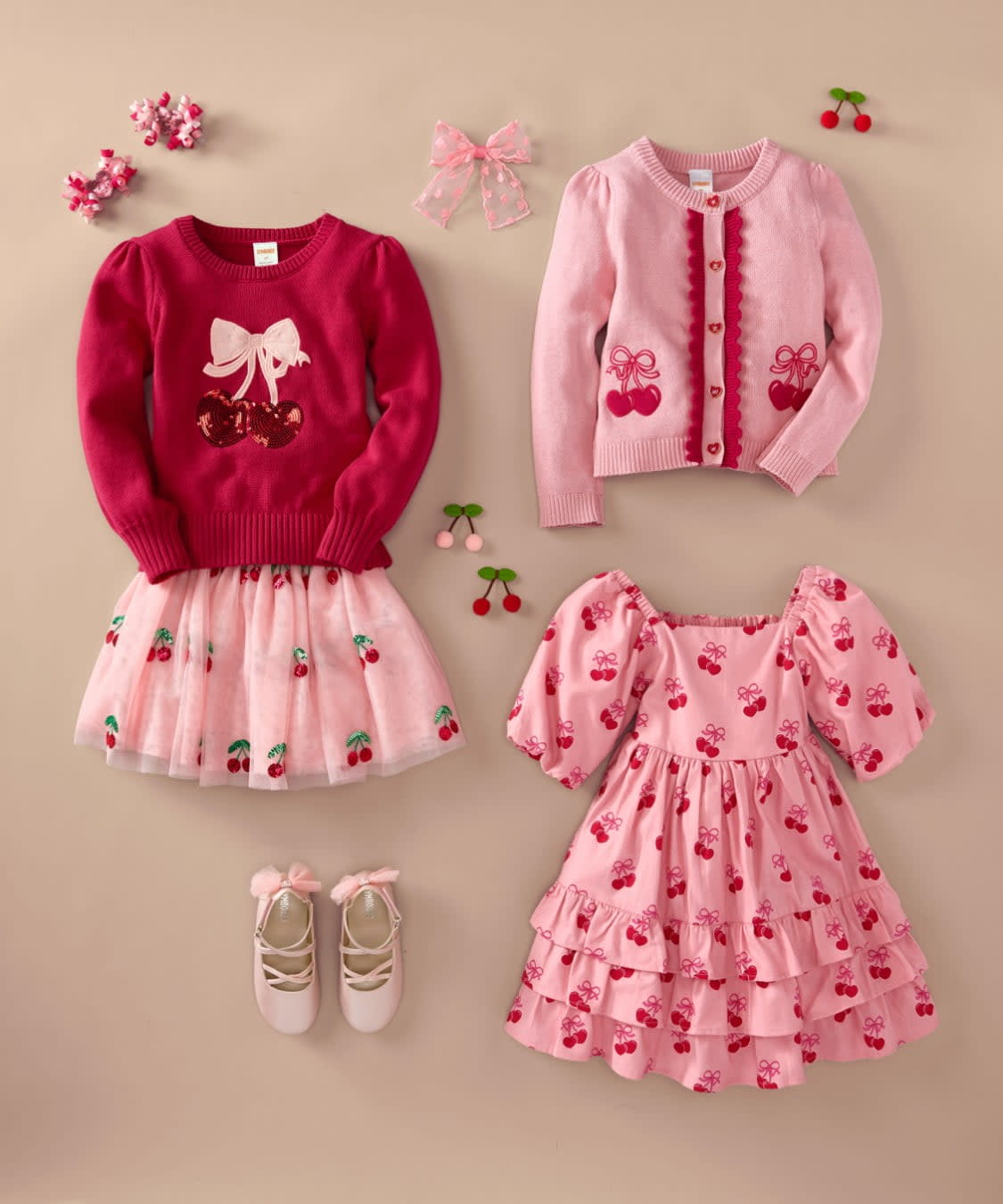 A collection of various pink and red children's clothing items, including a sweater, cardigan, skirt, and shoes, arranged on a light-colored background.