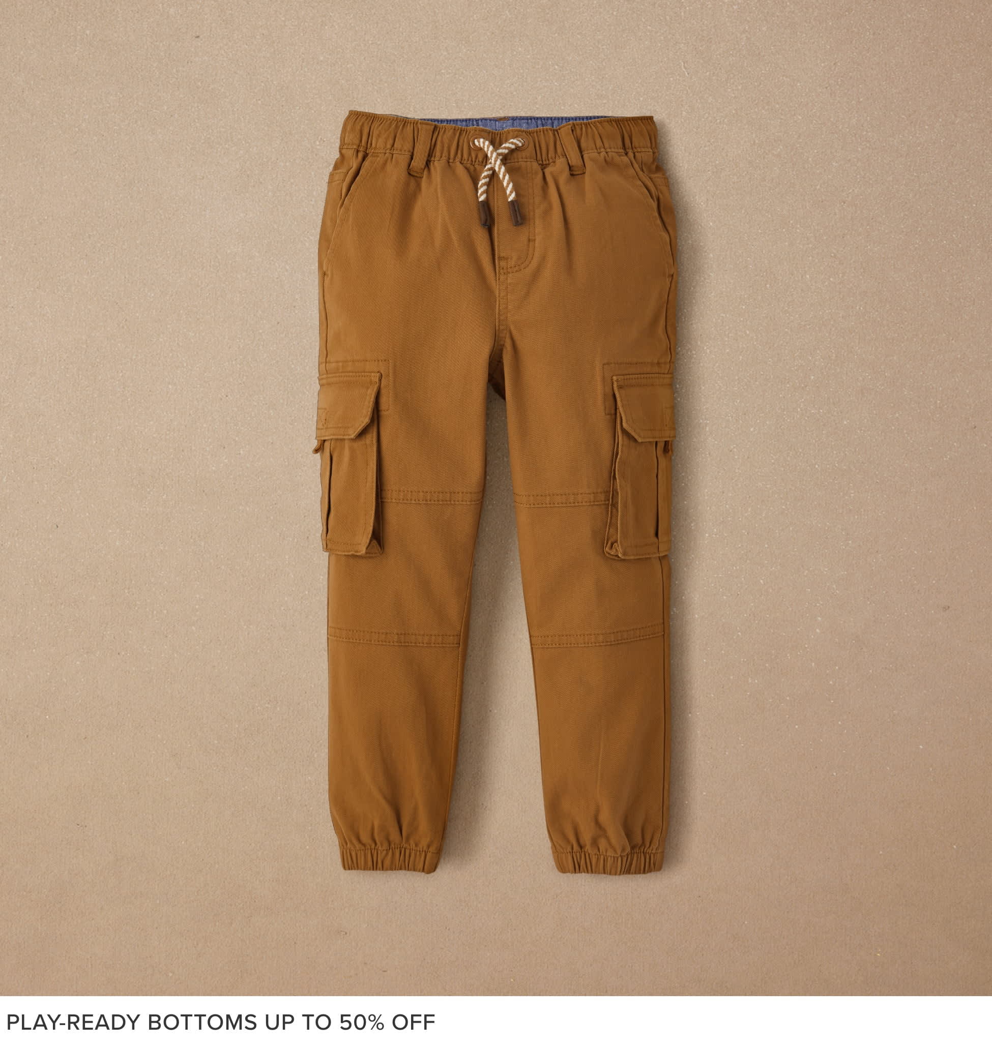 A pair of tan cargo pants with drawstring waist and pockets, against a plain beige background.