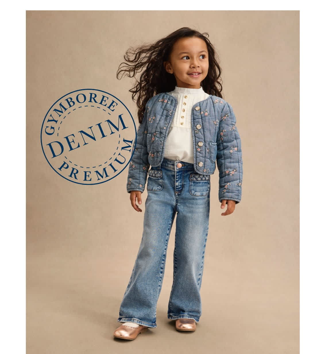A young girl with curly hair is wearing a denim jacket and jeans, standing in front of a beige background with a "Gymboree Denim Premium" logo.