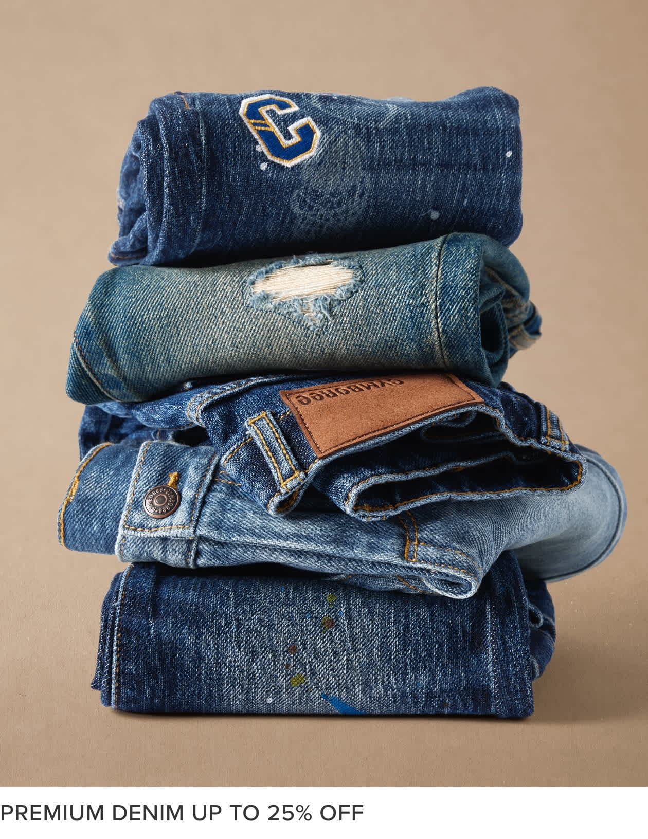 A stack of various denim clothing items, including jeans, jackets, and a towel, against a beige background.